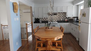 Une cuisine spacieuse avec des meubles blancs, une table à manger en bois et un luminaire suspendu.