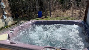 Un bain à remous doté d’un panneau de commande, entouré d’une terrasse en bois et d’un mur en briques.