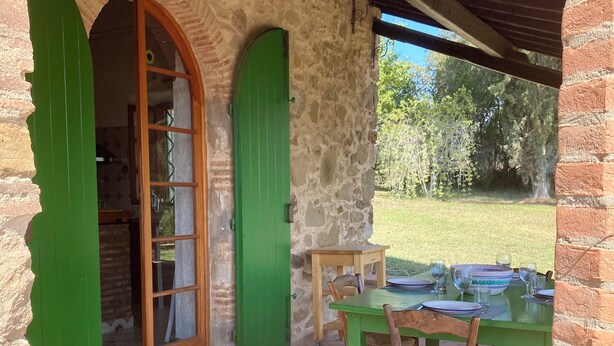 A stone building with green doors and a patio area with a table set for dining.