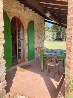 Un bâtiment en pierre avec des portes vertes et un patio agrémenté d’une table dressée pour le repas.