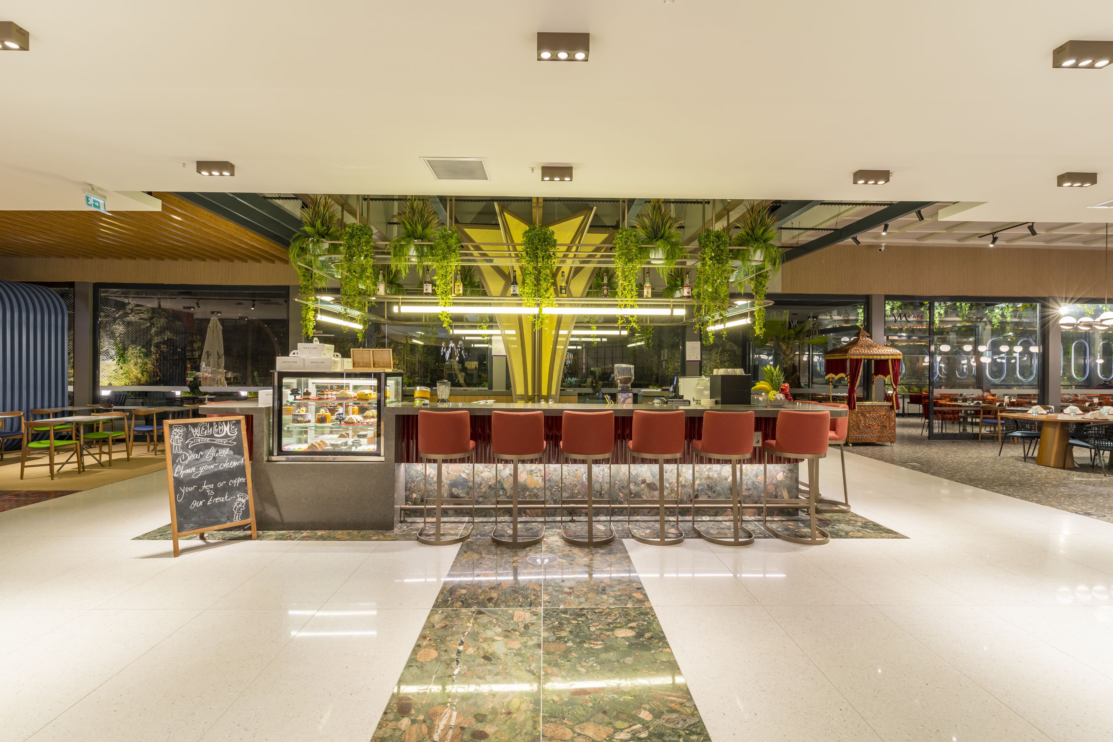 Un área de bar moderna con un arreglo central de plantas, taburetes y una pizarra.