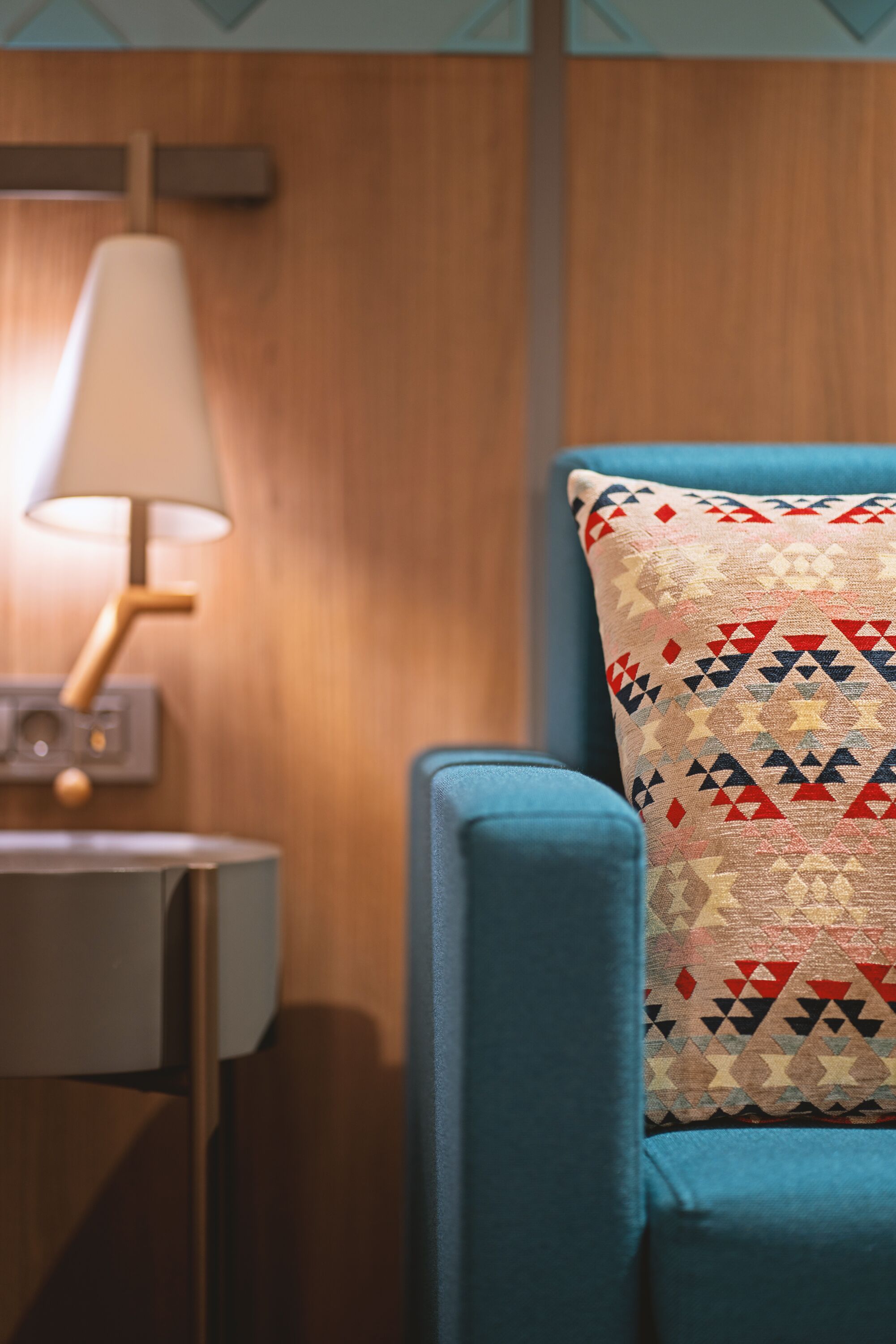 A room with a blue armchair, a patterned pillow, and a lamp on a side table.