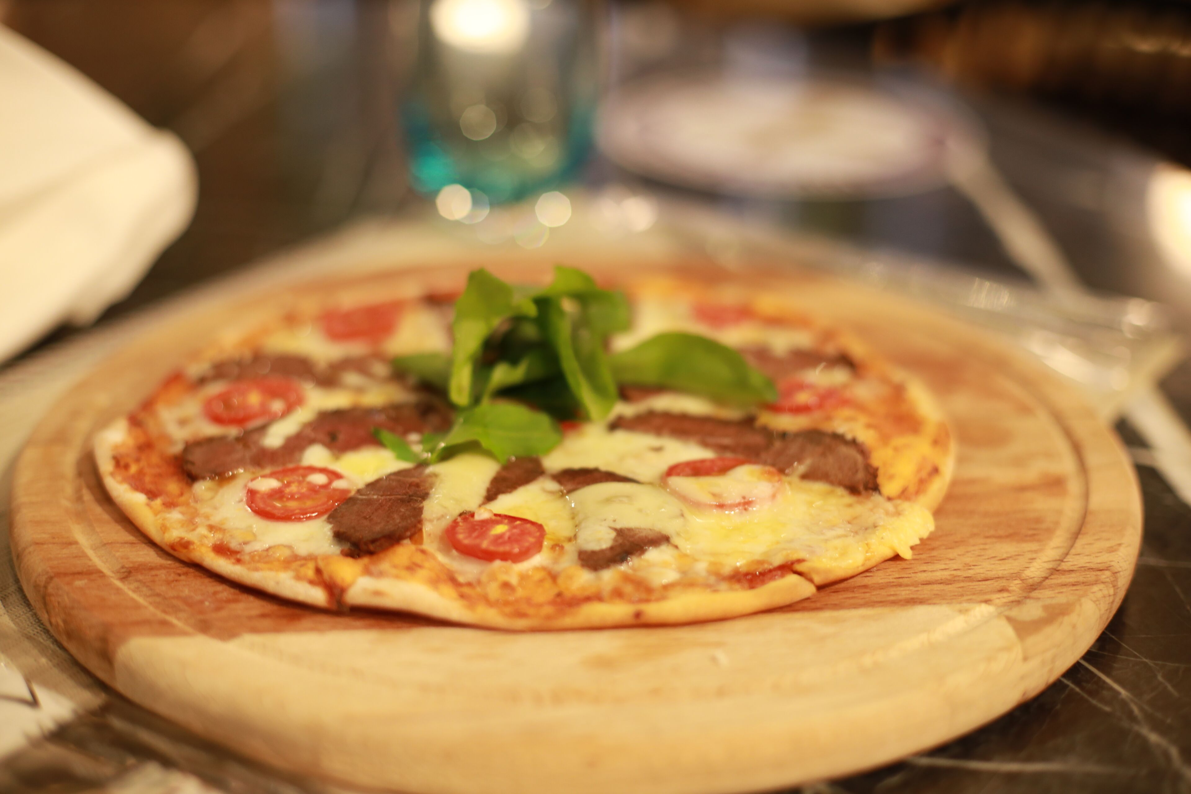 Una pizza sobre una tabla de madera con ingredientes como tomates, queso y vegetales verdes.