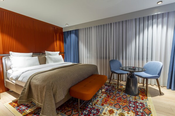 Una habitación de hotel moderna con una cama, un banco, una pequeña mesa y sillas.