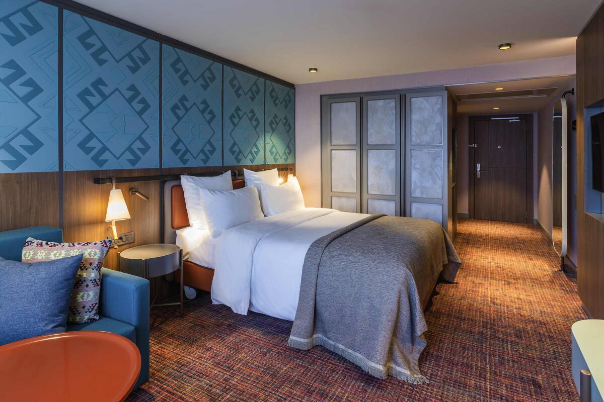 Ein Hotelzimmer mit einem Bett, einem blauen Sessel, einem Nachttisch und einer Wand mit Muster.