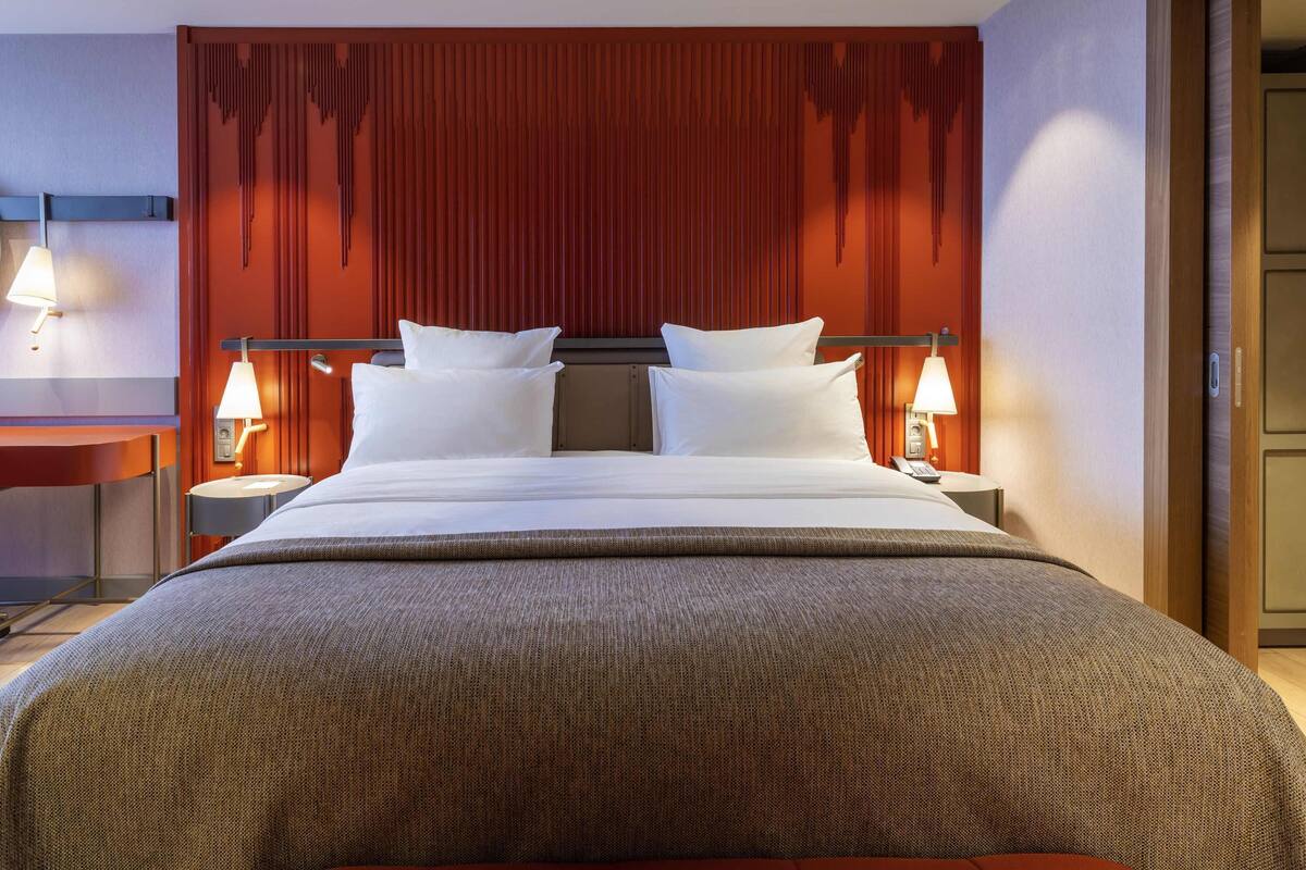 Ein Hotelzimmer mit einem Bett, zwei Nachttischen mit Lampen, einem Holz-Kopfteil und einer Tür.