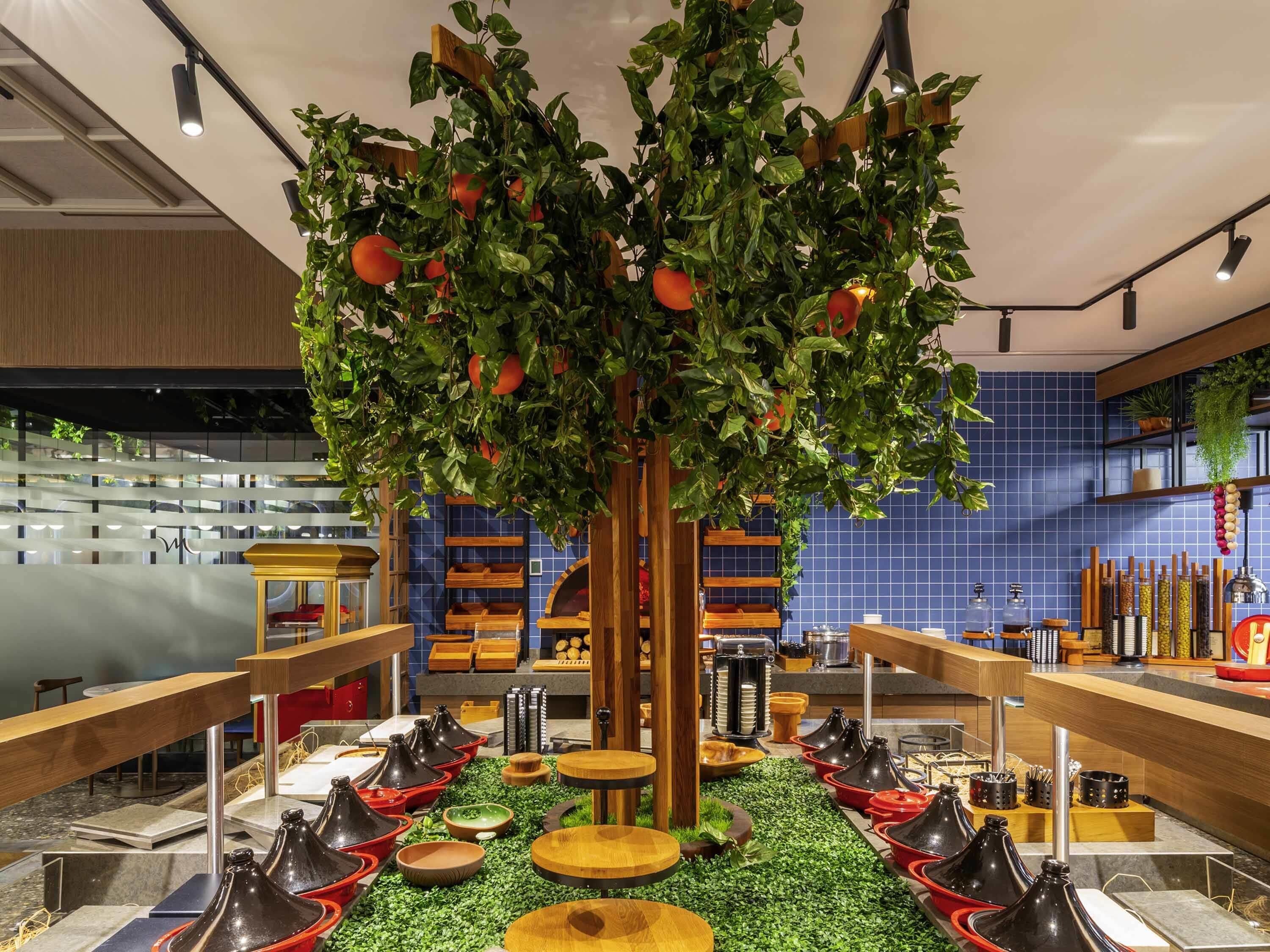 A restaurant with a central tree adorned with red fruits, surrounded by dining tables and chairs.
