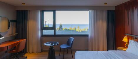 A hotel room with a bed, desk, chair, and a view of the sea.
