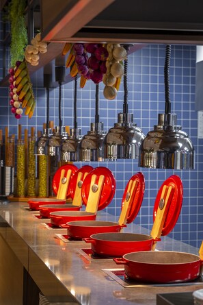 Une cuisine dotée de plans de travail en acier inoxydable, d’ustensiles de cuisine rouges, d’accessoires suspendus et d’un dosseret de carrelage bleu.