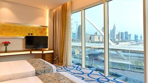 Habitación de hotel con un ventanal grande, un televisor de pantalla plana, una cama y un panel decorativo en la pared.
