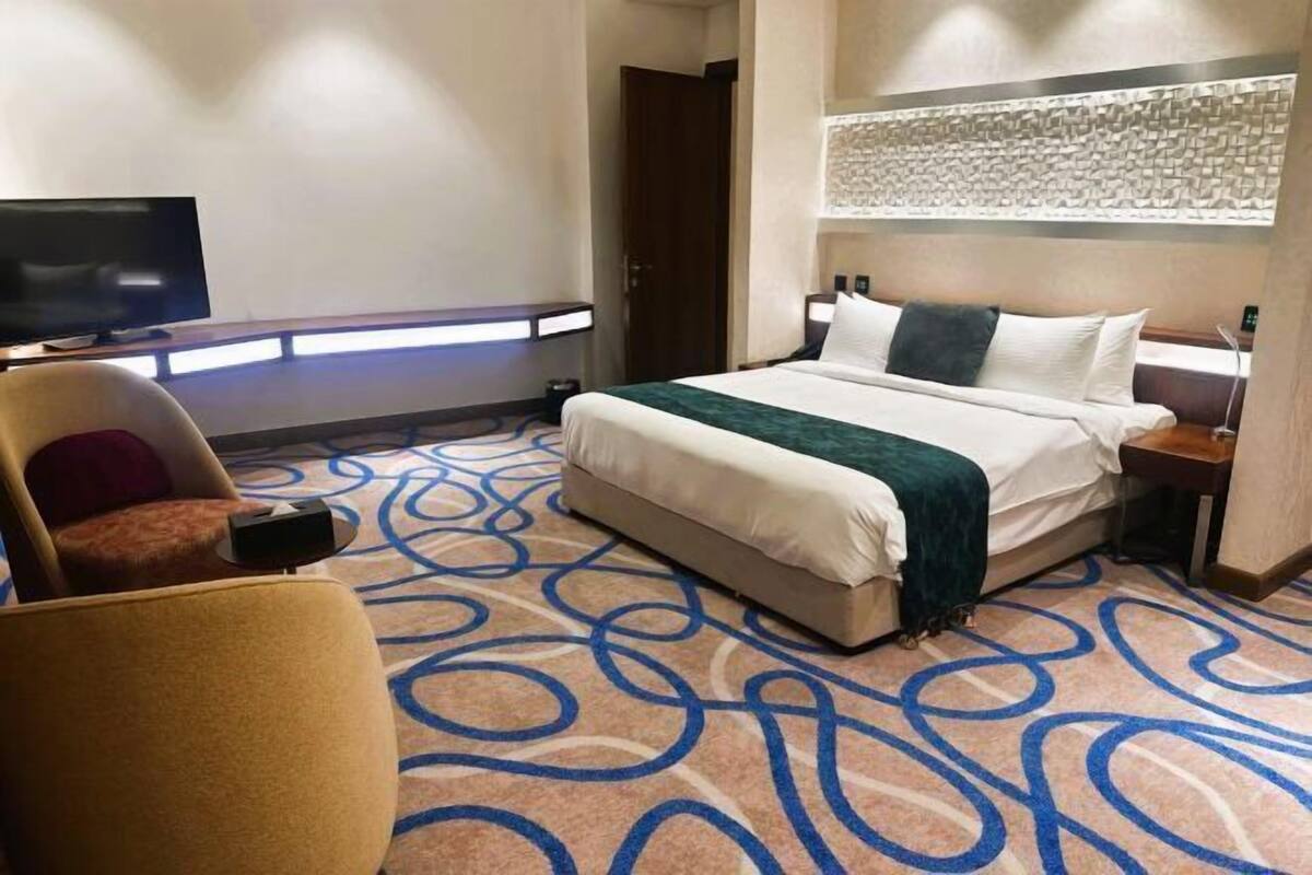 A hotel room with a bed, a TV, a chair, a nightstand, and a patterned carpet.