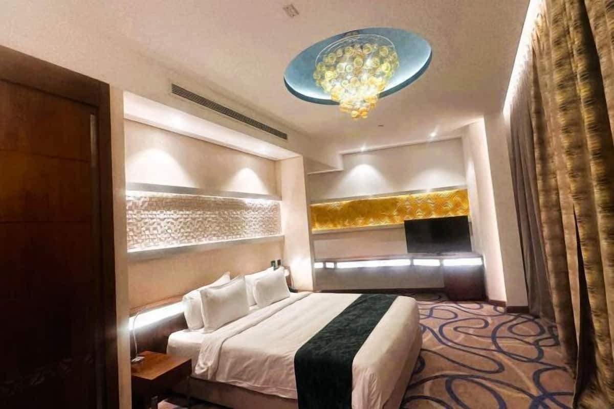 A hotel room with a bed, bedside tables, a TV, and a patterned carpet.