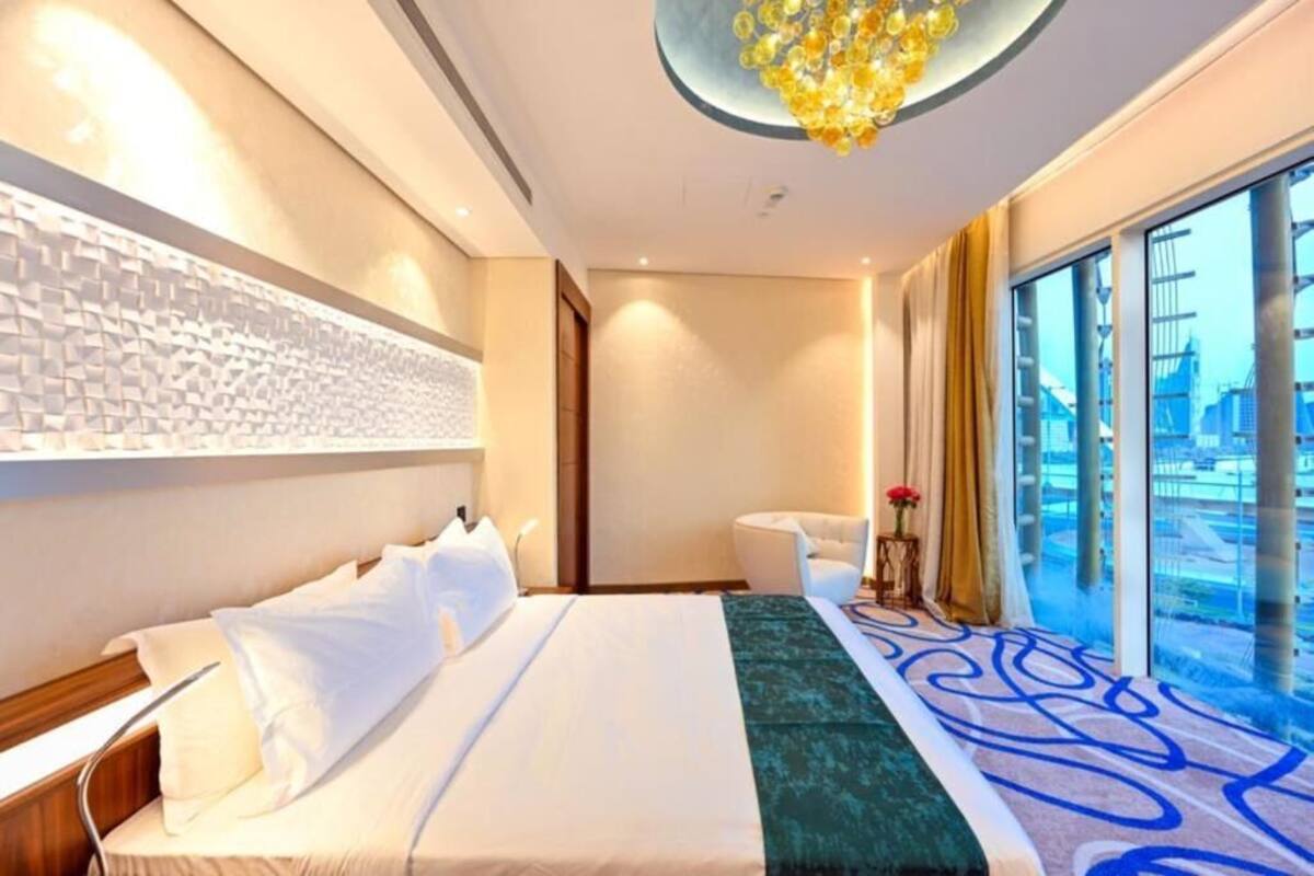 A hotel room with a large bed, a sitting area, a decorative wall, and a view through large windows.