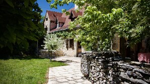 A stone building with a red roof, a stone wall, and a paved pathway leading to a door. - Charming air-conditioned house with heated fenced swimming pool and large garden (Espédaillac)