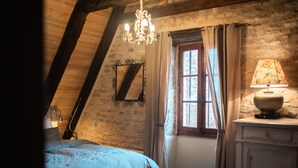 A bedroom with a sloped ceiling, a bed, a chandelier, a window with curtains, and a lamp on a dresser. - Charming air-conditioned house with heated fenced swimming pool and large garden (Espédaillac)