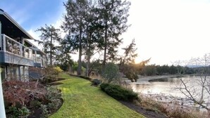 A pathway leading to a building with a view of a lake and trees. - Oceanfront Nanoose Bay stunning views condo sleeps 6 (Nanoose Bay)