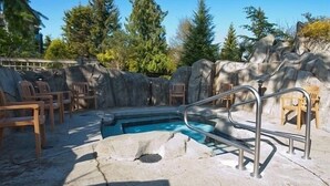 A pool area with a stone wall, wooden chairs, and a metal pool ladder. - Oceanfront Nanoose Bay stunning views condo sleeps 6 (Nanoose Bay)