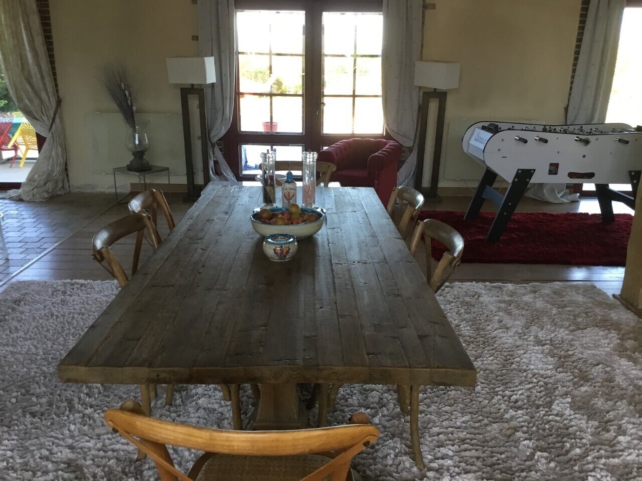 Une salle à manger avec une table en bois, des chaises et un saladier rempli de fruits.