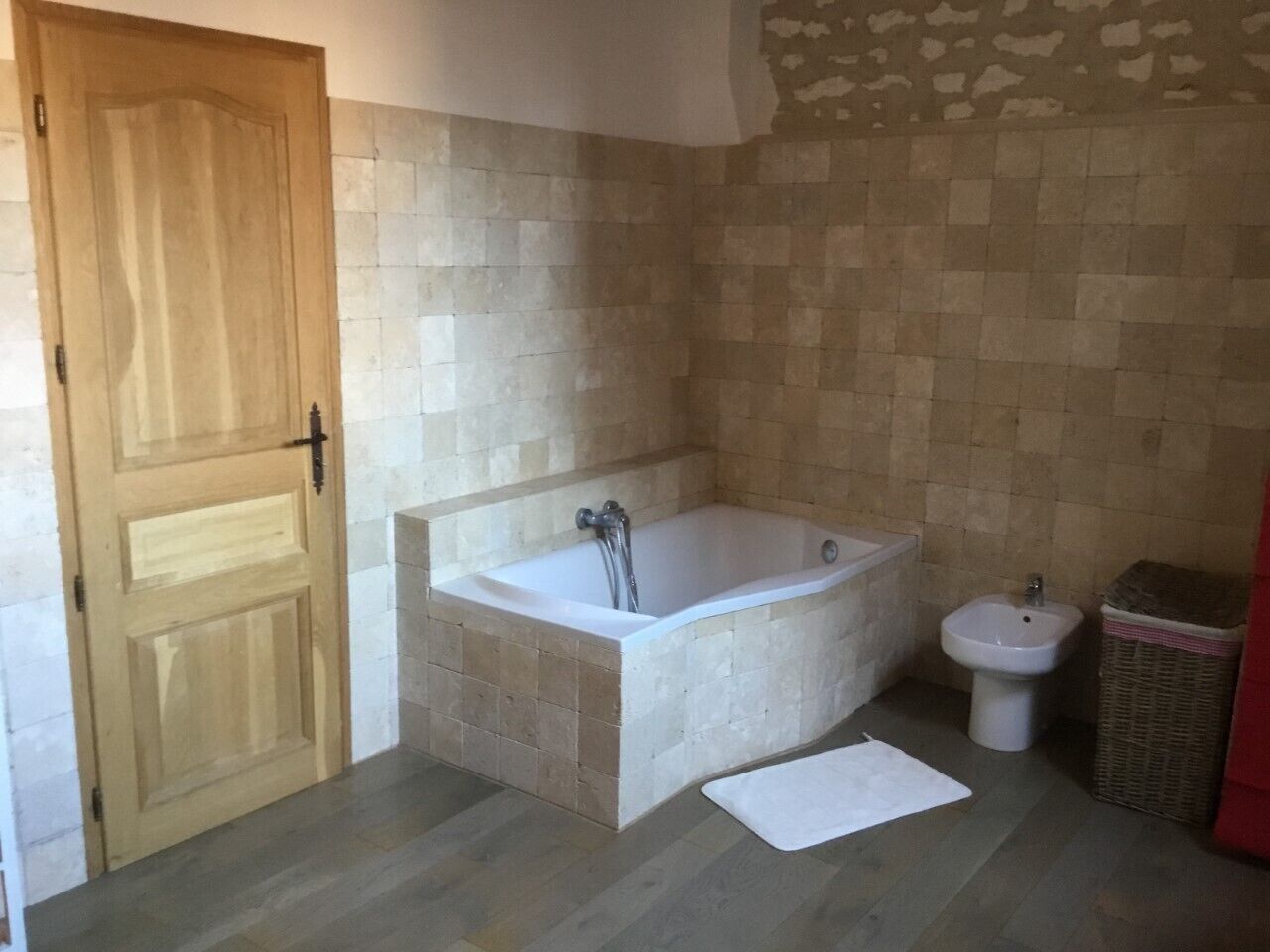 A bathroom with a wooden door, a freestanding bathtub, a bidet, and a wicker basket.
