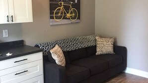 A living room with a black sofa, a white cabinet, and a framed picture of a bicycle. - Lauren's Loft in Historic Downtown Pleasant Hill (Pleasant Hill)