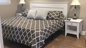 A bedroom with a bed, two bedside tables, a nightstand, a lamp, an air conditioner, and a window with blinds. - Lauren's Loft in Historic Downtown Pleasant Hill (Pleasant Hill)