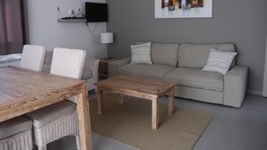 A living room with a sofa, two chairs, a coffee table, a TV mounted on the wall, and a painting. - 4* apartment facing the Luberon (Oppède)