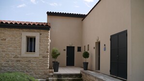 A courtyard with a stone building, a black door, and two potted trees. - 4* apartment facing the Luberon (Oppède)