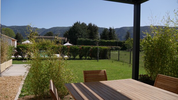 A wooden table and chairs under a pergola with a view of a grassy yard and mountains in the background. - 4* apartment facing the Luberon (Oppède)