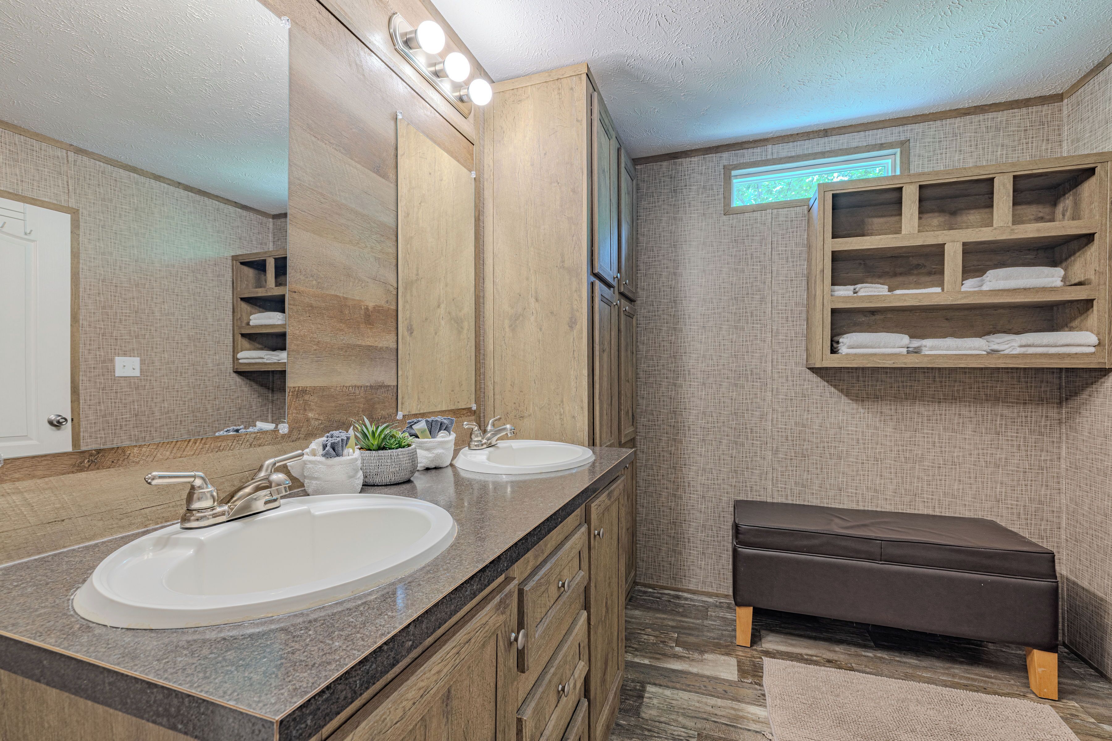 A bathroom with two sinks, wooden cabinets, a bench, and a towel rack.
