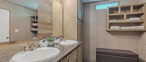 A bathroom with two sinks, wooden cabinets, a bench, and a towel rack.