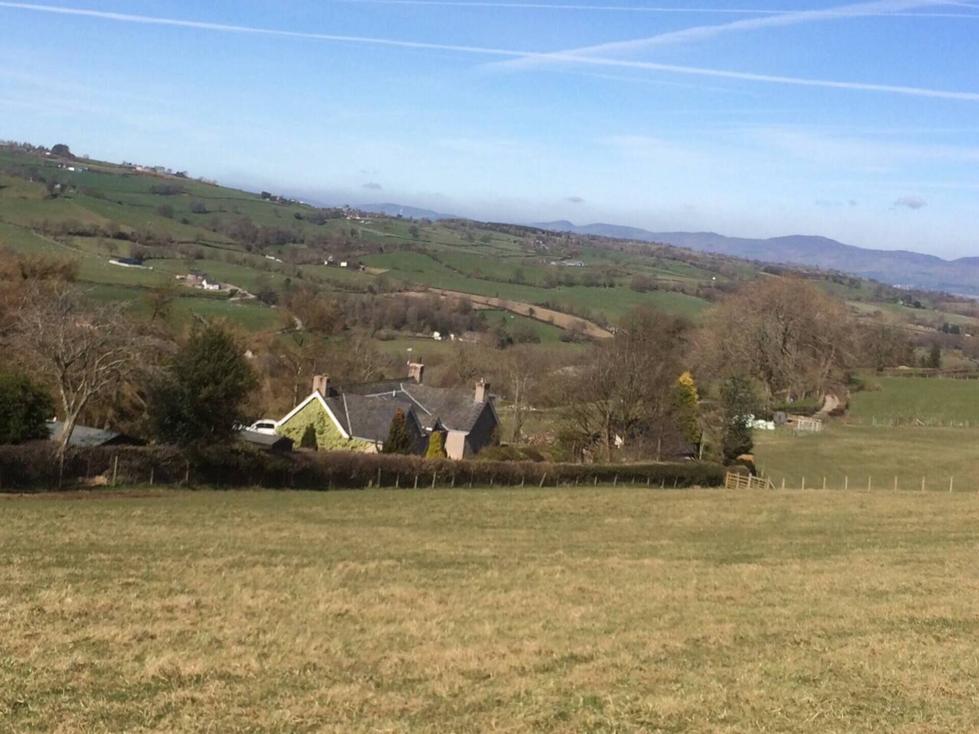A rural landscape with rolling hills, a few houses, and a clear sky.
