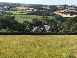 A rural house with a sloped roof, surrounded by fields and trees.