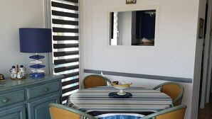 Un comedor con una mesa a rayas, sillas de mimbre, un armario azul y una ventana con persianas.