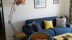 Una sala de estar con una mesa a rayas, un sofá azul con cojines, una lámpara de pie y un cuadro en la pared.