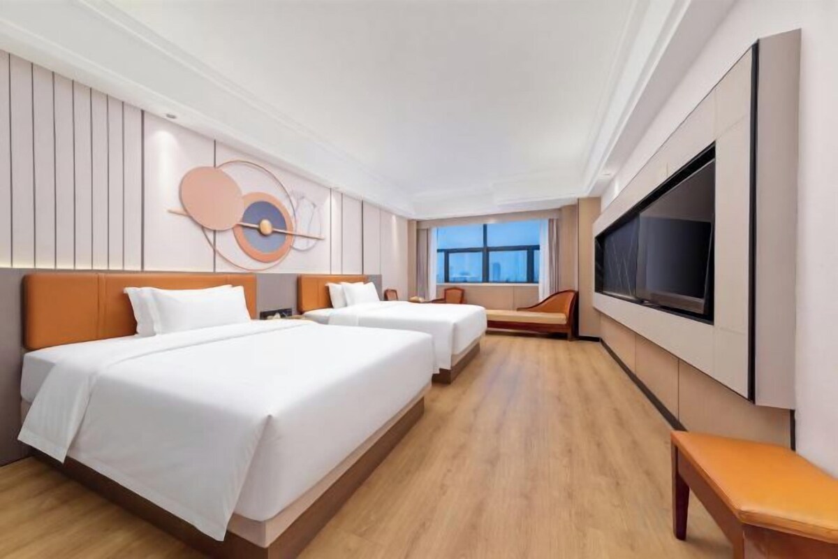 A hotel room with two beds, a large TV, and a window with a view.
