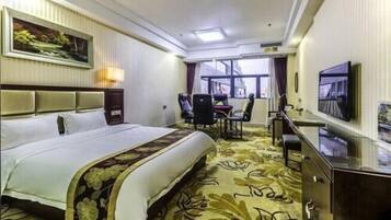 A hotel room with a large bed, a desk with a chair, a television, and a window with curtains.