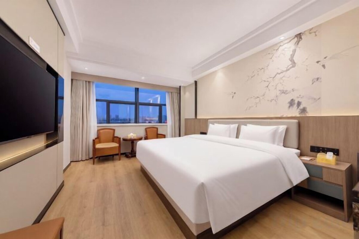 A hotel room with a large bed, a television, a desk, and a window with a view.