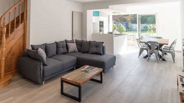 Un salon moderne avec un canapé d’angle gris, une table basse en bois et un escalier.