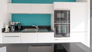 Une cuisine moderne avec des armoires blanches, un mur d’accent de couleur turquoise, un évier en acier inoxydable, une machine à café et un four encastré.