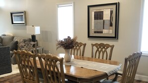 Een eethoek met een houten tafel en stoelen, een vaas met gedroogde bloemen en een kunstwerk in een lijst aan de muur.