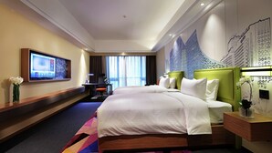 Habitación de hotel con una cama grande, un escritorio, un televisor montado en la pared y vistas a la ciudad a través de la ventana.