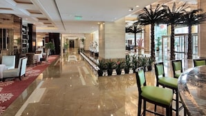 A spacious lobby with a polished marble floor, a reception desk, and a seating area with green upholstered chairs. - Best Western Ridong Garden Hotel (Xiamen)