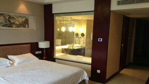 A hotel room with a large bed, a bedside lamp, a bathroom with a large mirror, and a painting on the wall. - Best Western Ridong Garden Hotel (Xiamen)