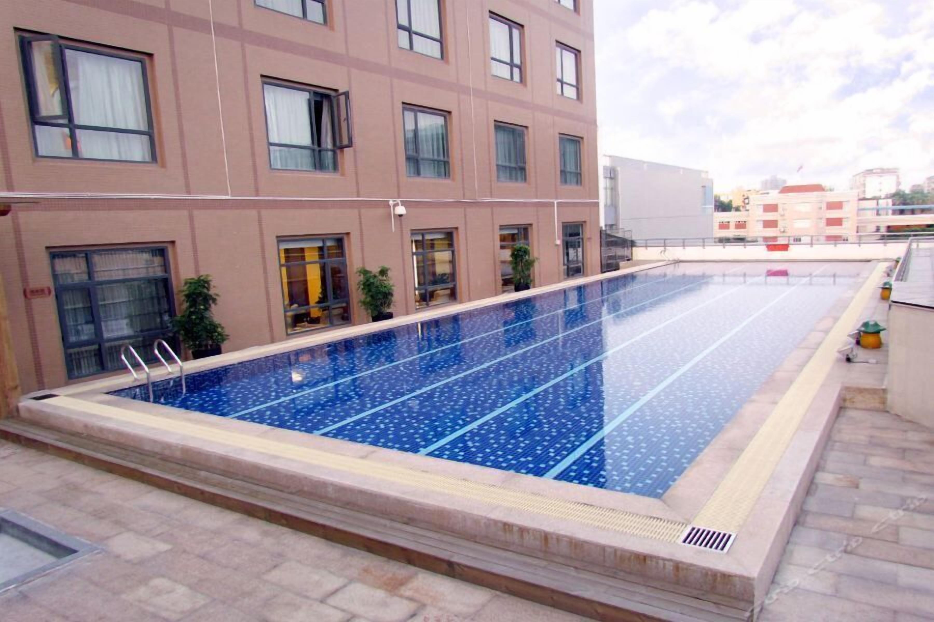 En pool på taket med blå kakelplattor, omgiven av en beige byggnad med många fönster och balkonger.