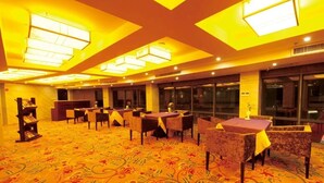 Een hotelentree met meerdere tafels en stoelen, een kamerbreed tapijt en grote ramen.