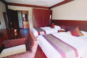 A hotel room with two beds, a wooden wardrobe, and a seating area.