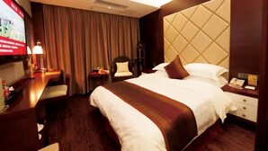 Een hotelkamer met een groot bed, een bureau met een computer, een stoel, een televisie en een nachtkastje met een lamp.