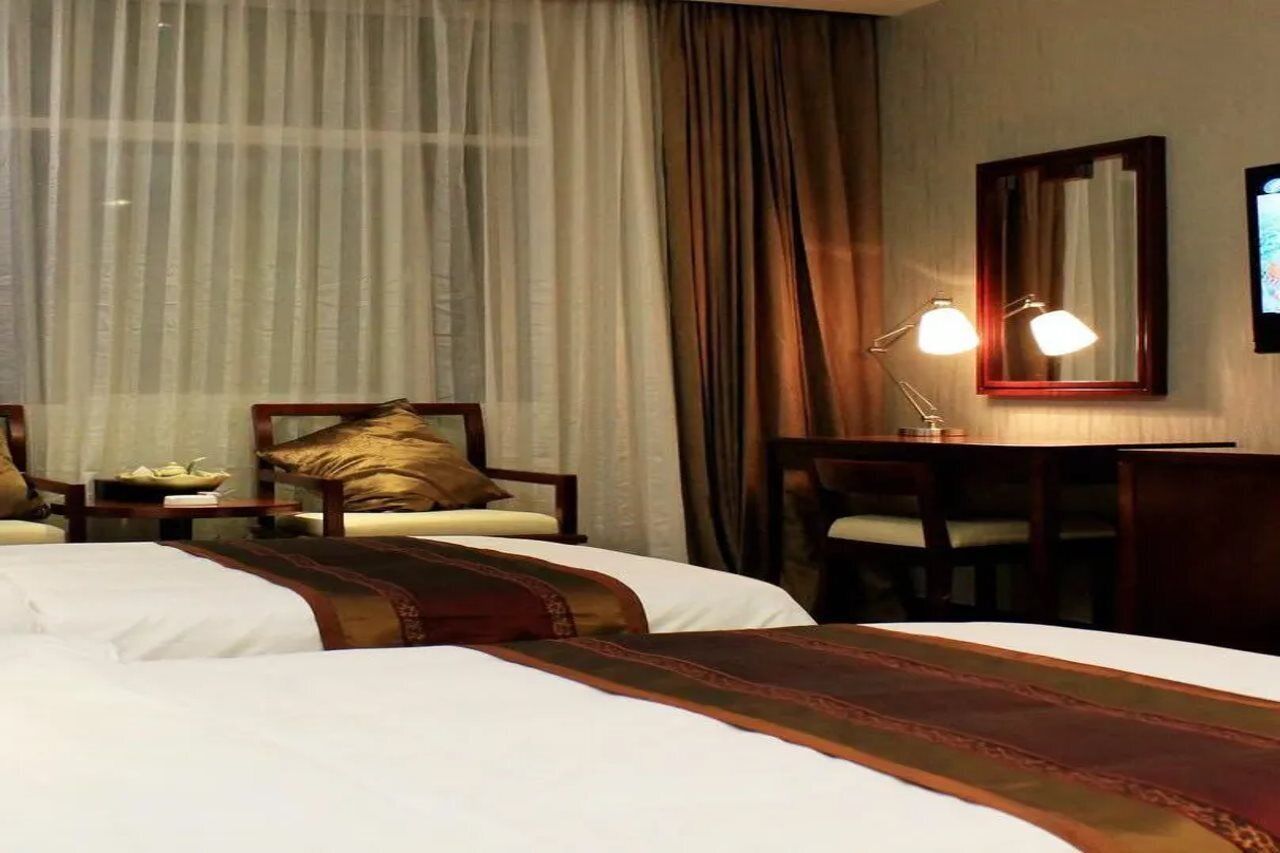 Ein Hotelzimmer mit zwei Betten, einem Schreibtisch, einem Stuhl, einer Lampe und einem Fernseher.