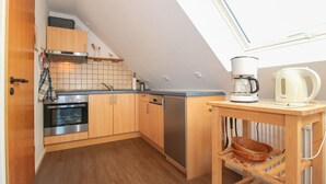 Una cocina compacta con armarios de madera, horno empotrado, lavavajillas y cafetera sobre una pequeña mesa de madera.