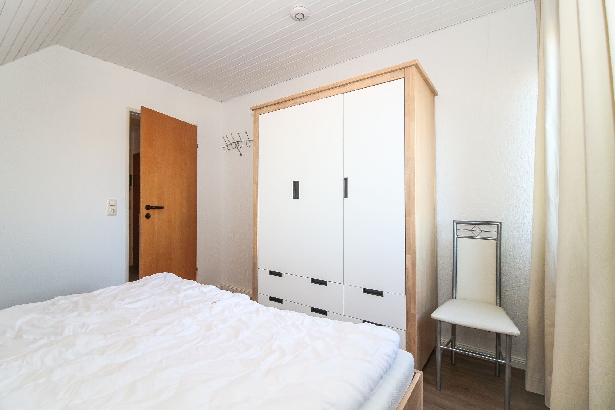 Ein Schlafzimmer mit Bett, Kleiderschrank, Stuhl und Tür.